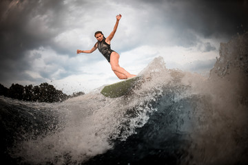 Sporty girl riding on the wakeboard on the river in the background of trees rising hands