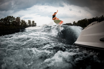 Sporty girl jumping on the wakeboard on the river on the wave of the motorboat