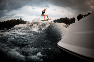 Slim fit girl jumping on the wakeboard on the river on the wave of the motorboat