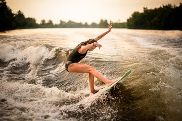 Skinny girl making a trick on the wakeboard on the river in the sunset