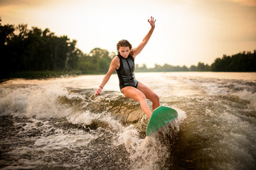 Girl making a trick on the green wakeboard on the river in the sunset