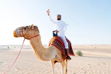 Foto op Canvas Arabian man with traditional clothes riding his camel © oneinchpunch