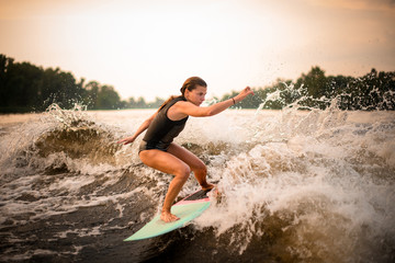 Woman making a trick on the green wakeboard on the river in the sunset