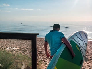 Portrait of a surfer with SUP board on the beach. Young man in sea, Extreme sport concept.