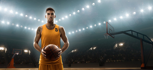 Young professional basketball player on a floodlit sports arena with the ball