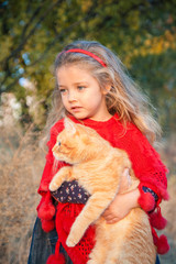 Portrait of a little girl with a red cat in her hands in autumn.