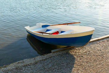 Naklejka premium A blue-and-white rowing boat is half pulled up on the shore of the lake.
