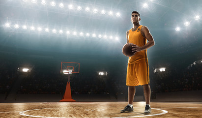 Young professional basketball player on a floodlit sports arena with the ball