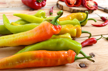A pile of pepper on a wooden table. Hot green, orange pepper. Rustic style.