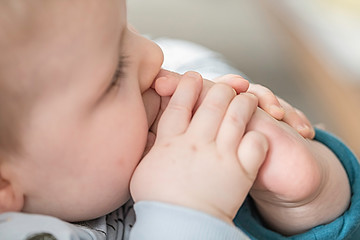 Cute baby taking feet in mouth. Adorable little baby boy sucking foot.