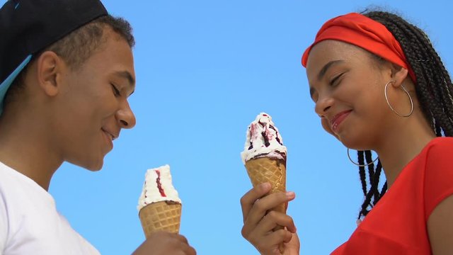 Smiling mix-raced teen couple enjoying ice-cream, summer date, bottom view