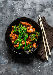 Teriyaki stir fry chicken with broccoli on dark background, top view. Asian style food