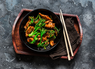 Teriyaki stir fry chicken with broccoli on wooden tray on dark background, top view