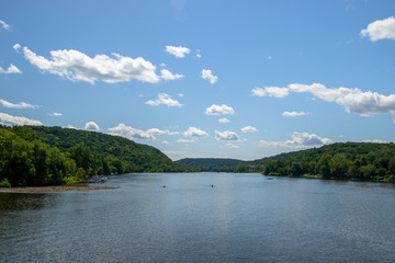 Wide angle view of the Delaware River near New Hope, Pennsylvania showing a wide body of deep blue water with tree covered hills in the background. There are boaters seen on the river
