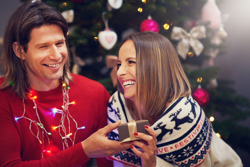 Obraz na płótnie Canvas Beautiful adult couple with present over Christmas tree