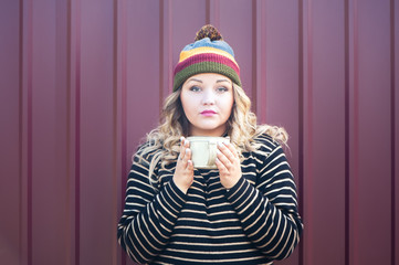 Expressive girl in a juicy autumn hat with cup of tea in her hand. Theme of autumn, bright colors and beauty. Bright photo of a beautiful girl in an autumn hat and a sweater on a stylish background