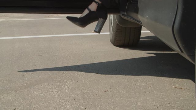 Slim female legs in trendy black high heel shoes getting out of parked car and gracefully walking away. Low section of beautiful wealthy woman in high heels stepping out of car.