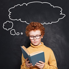 Child boy reading a book on school chalkboard background with empty speech clouds bubbles