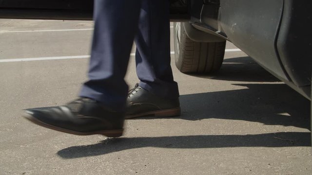 Close-up of male legs in elegant black shoes and suit exiting parked luxury car. Low section of wealthy businessman in trendy suit and shoes getting out of parked vehicle and walking away.