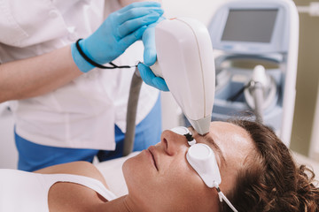 Cropped shot of a cosmetologist removing facial hair of a female client. Woman getting laser hair...