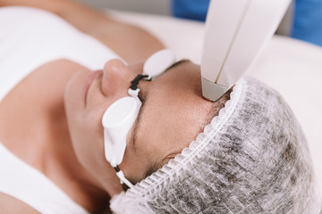 Cropped close up of a woman getting laser hair removal on her forehead. Cosmetologist perfecting...
