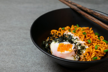 Drunken spicy noodles in black bowl with Onsen egg on the concrete table.