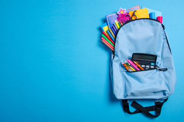 Back to school concept. Blue backpack with school supplies on blue background. Top view. Copy space