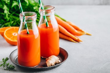 Fresh carrot, ginger and orange drink in glass bottles on a gray stone background