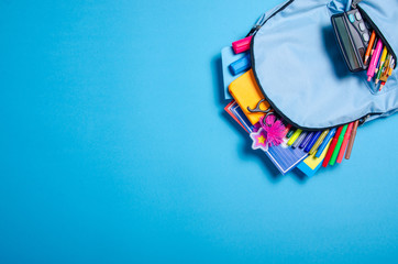 Back to school concept. Blue backpack with school supplies on blue background. Top view. Copy space