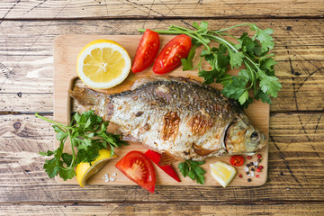 Baked carp fish with vegetables and spices on a wooden table.