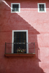 Metal wrought iron balcony with flowers on the coral color wall. Traditional spanish house in the city of Palm de Mallorca, Spain.