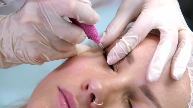 Beauty clinic. Eyelash extension procedure. Portrait of attractive young woman in the cosmetology clinic. Professional stylist lengthening female lashes. 