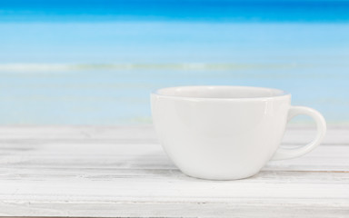 Coffee cup on white wood table with bright blue sea background