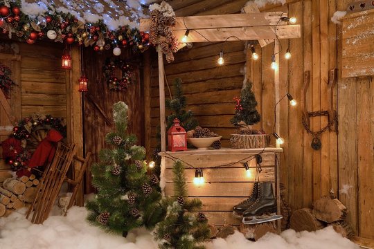 New Year's photo zone with snow near a wooden house. Christmas decor: toys, Christmas trees, skis, garland, firewood, glowing light bulbs. festive mood. picture for postcard