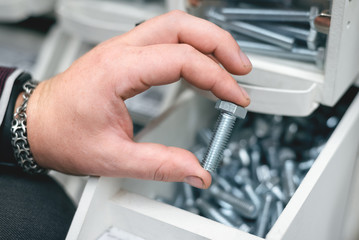 A buyer is choosing a bolt. A man is holding in hand one silver screw.