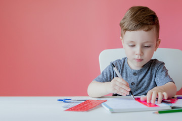 Portrait of cute kid boy at home making homework. Little concentrated child writing with colorful...