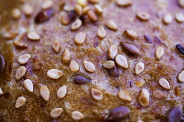 Macro close up of surface of german baked seeded grain bread roll with crispy brown crust multiple seeds