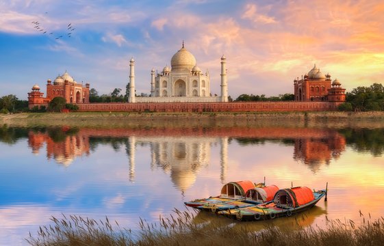 Taj Mahal Agra on the banks of river Yamuna at sunset with moody sky and view of wooden boats used for tourist ride on the river 