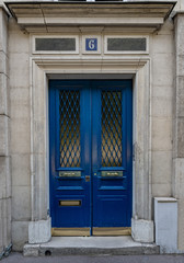 Vintage entrance and door windows with matte glass protected by rhombus patterned lattice. Bright blue painted antique door of old stone building in Paris France. Exterior of house in Europe