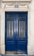 Fototapeta na wymiar Old blue door. Doorway with door windows with matte glass protected by vertical patterned grids. Dark blue painted antique door with shabby bottom part. Antique building in Paris France. 