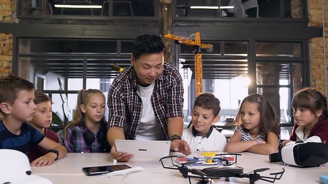 Team of six young caucasian curious technicians working together with their teacher using computer tablet in engineering class