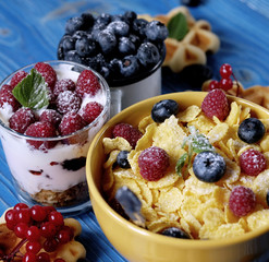 Healthy breakfast with corn flakes, berries, waffle and milk on blue background.