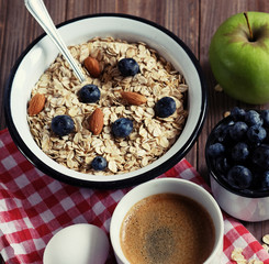 A healthy breakfast is a great start to a new day. Oatmeal porridge, coffee, apple, berries and nuts on a wooden table.