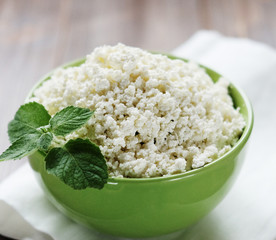 Cottage cheese with mint in a green bowl on a white napkin.