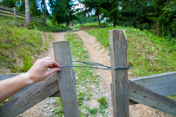 hand opens an old wooden gate. Against the background of the forest