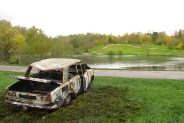 Burnt car in the woods by the lake. Criminals broke auto and burned in the pond. Damaged and thrown...