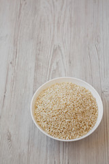 Organic Arborio rice in a white bowl on a white wooden background, low angle view. Copy space.