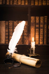 Inkwell with pen, scroll of parchment, and candle against the background of bookshelves with old books
