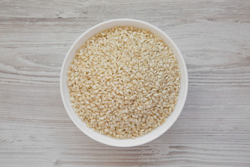 Organic Arborio rice in a white bowl on a white wooden surface, top view. Flat lay, overhead, from above. Close-up.