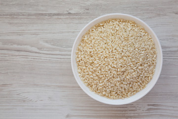 Organic Arborio rice in a white bowl on a white wooden background, top view. Flat lay, overhead, from above. Copy space.